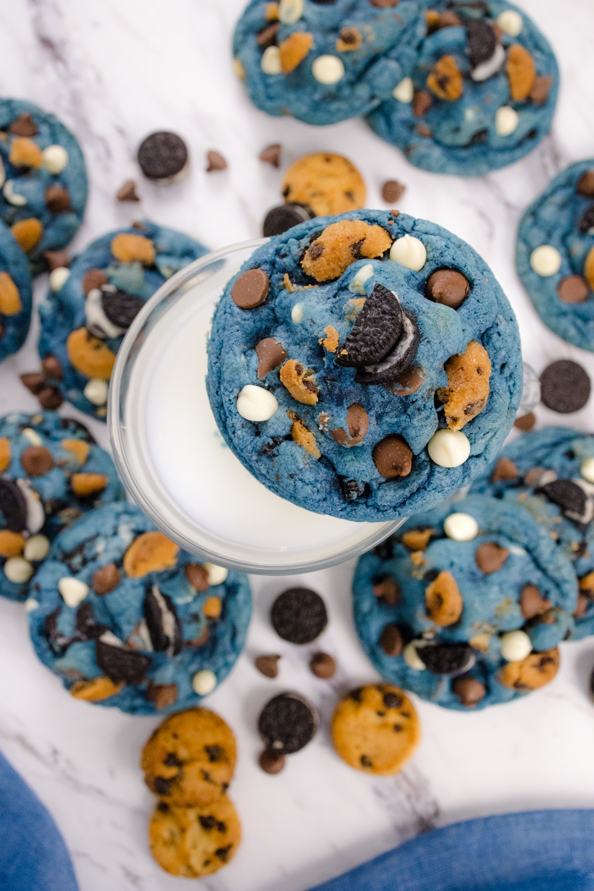 Top view of a cookie monster cookie sitting on the edge of a glass of milk, surrounded by more cookie monster cookies.