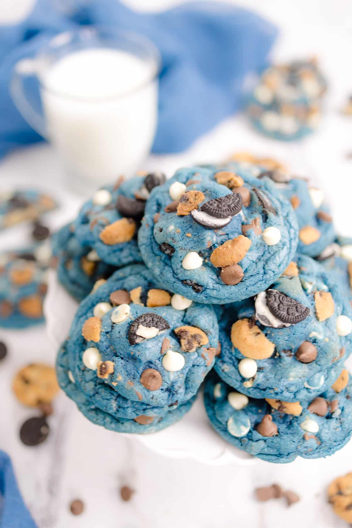 A stack of cookie monster cookies next to a glass of milk.