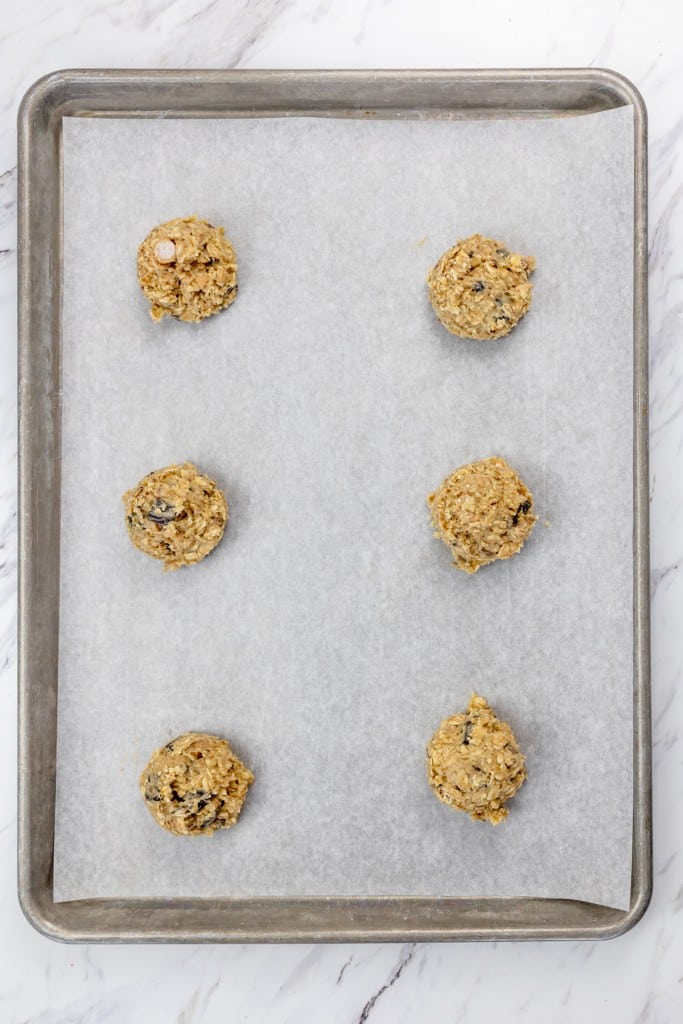 Top view of a baking tray lined with parchment paper with six cookie dough balls on it.