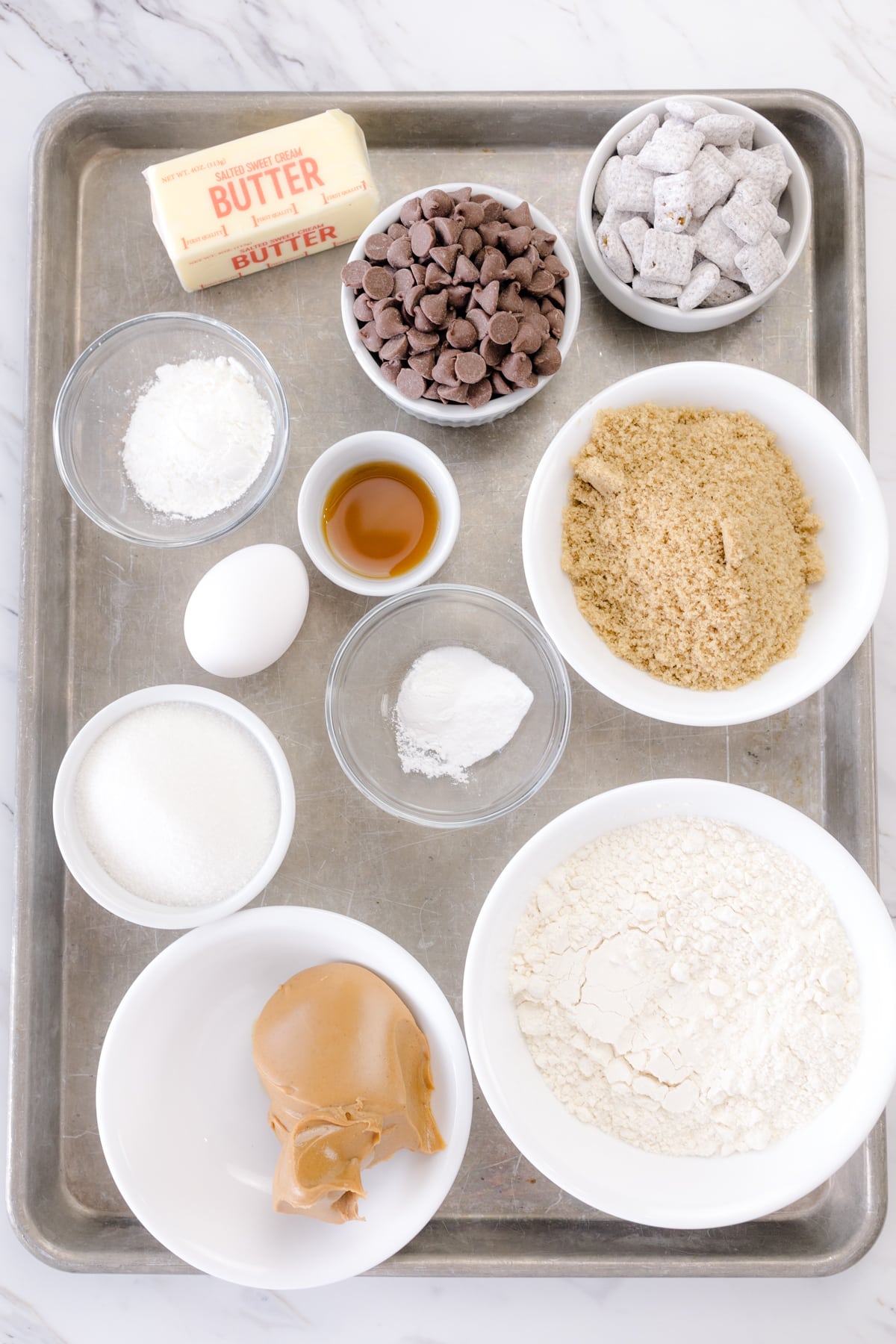 Top view of the ingredients needed to make Muddy Buddy Cookies in small bowls on a baking tray.