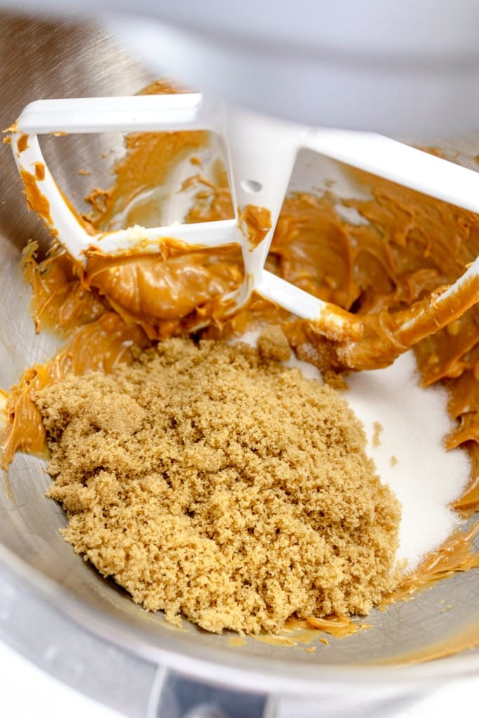 Close up of the bowl of a stand mixer with a paddle attachment with creamed peanut butter with sugars in it.