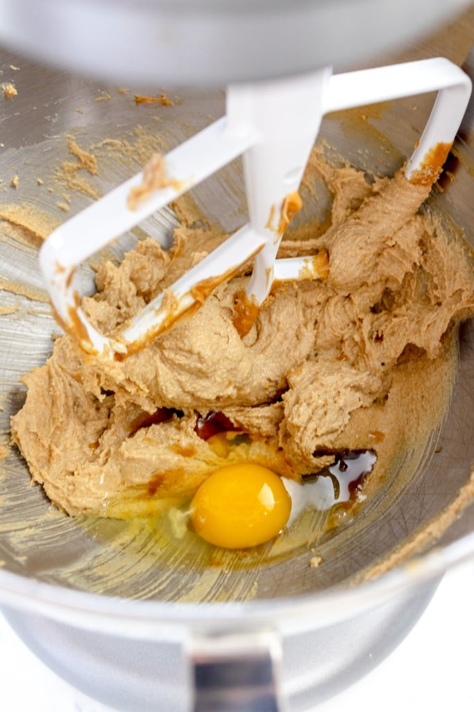 Close up of the bowl of a stand mixer with a paddle attachment with a creamed mixture and an egg on top.