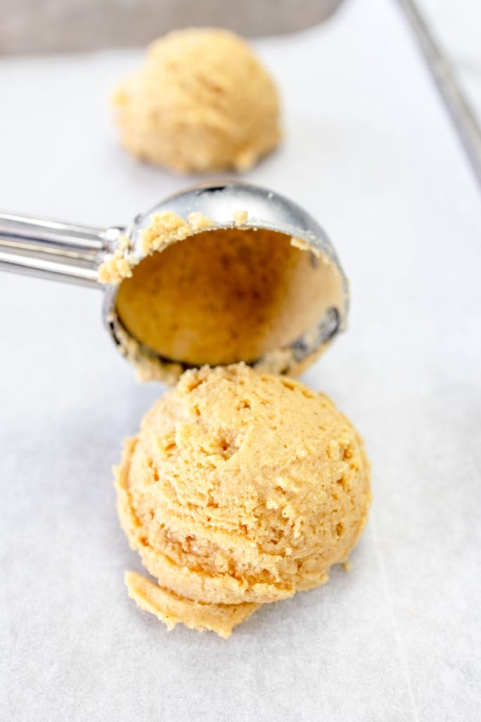 Close up of a cookie scoop putting a scoop of peanut butter cookie dough onto a parchment lined baking tray.