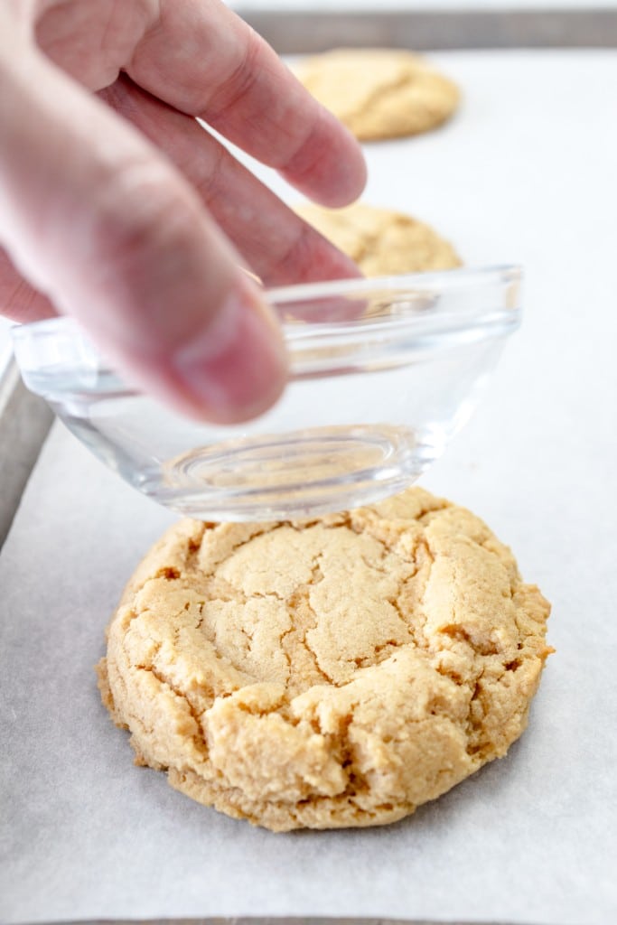 Close up of a small glass bowl making an indent in a freshly baked peanut butter cookie.