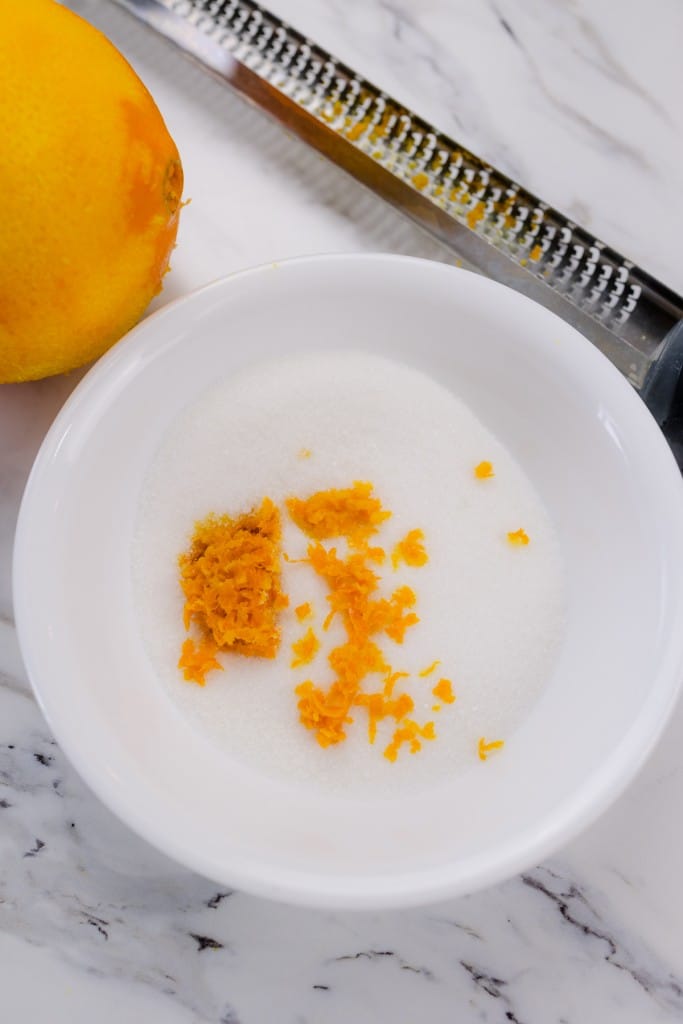 Top view of a small white bowl with sugar and orange zest in it.