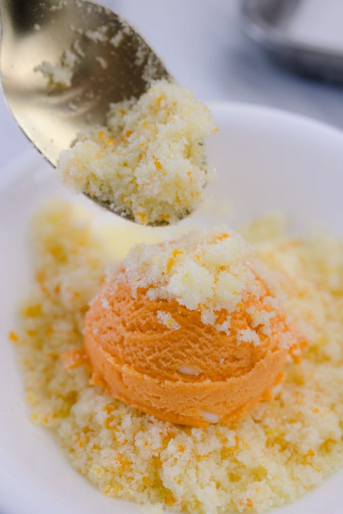 Close up of an orange cookie dough ball being coated in orange sugar.
