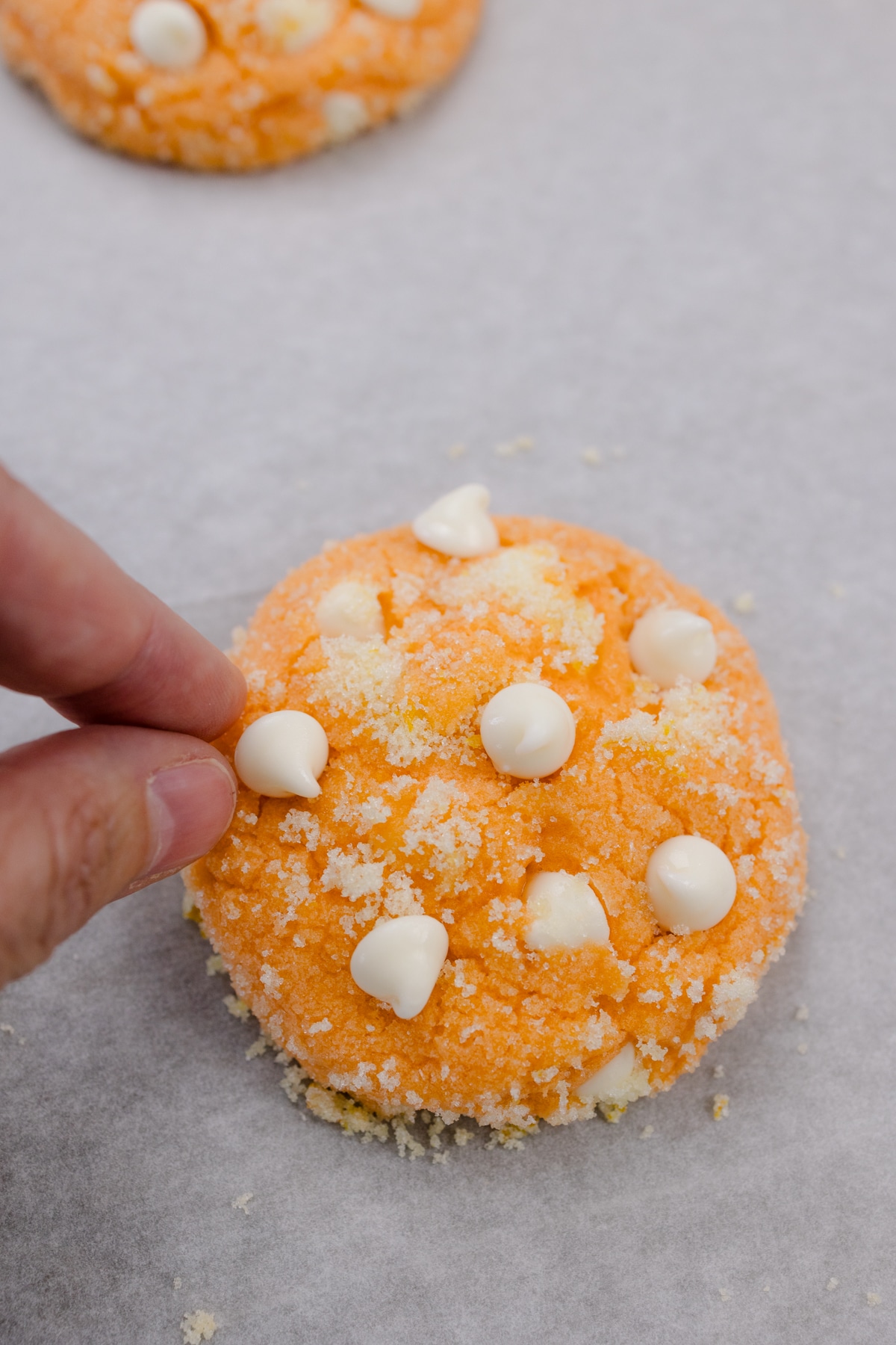 Close up of an orange creamsicle cookie with extra chocolate chips being added on top.