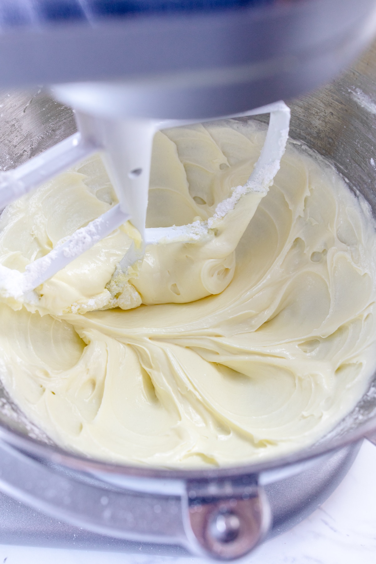 A large mixing bowl mixing together the creamed butter and sugar with egg, coconut extract, and cream.