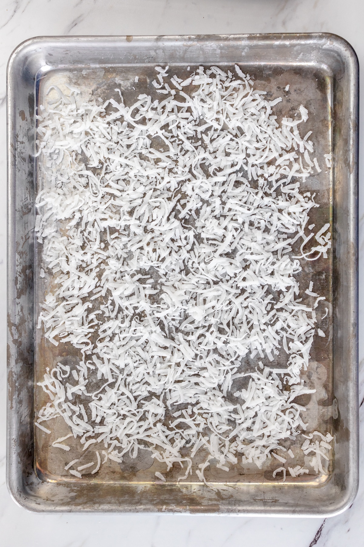 Top view of shredded coconut on a baking tray before being toasted.