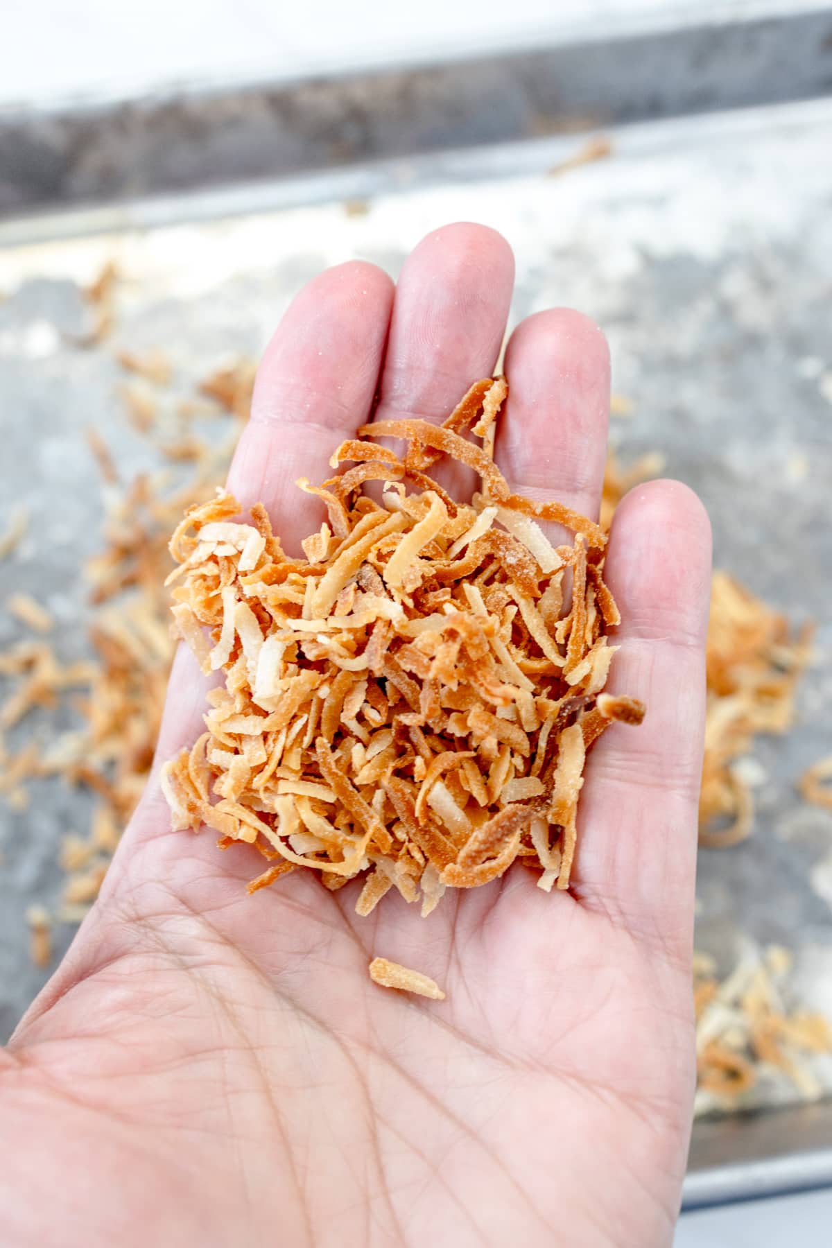 Close up of someone holding up a handful of shredded toasted coconut.