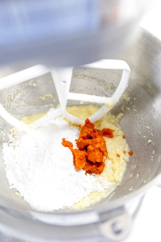 Close up of the bowl of a stand mixer with a creamed mixture in the bottom wit powdered sugar and pumpkin puree on top.