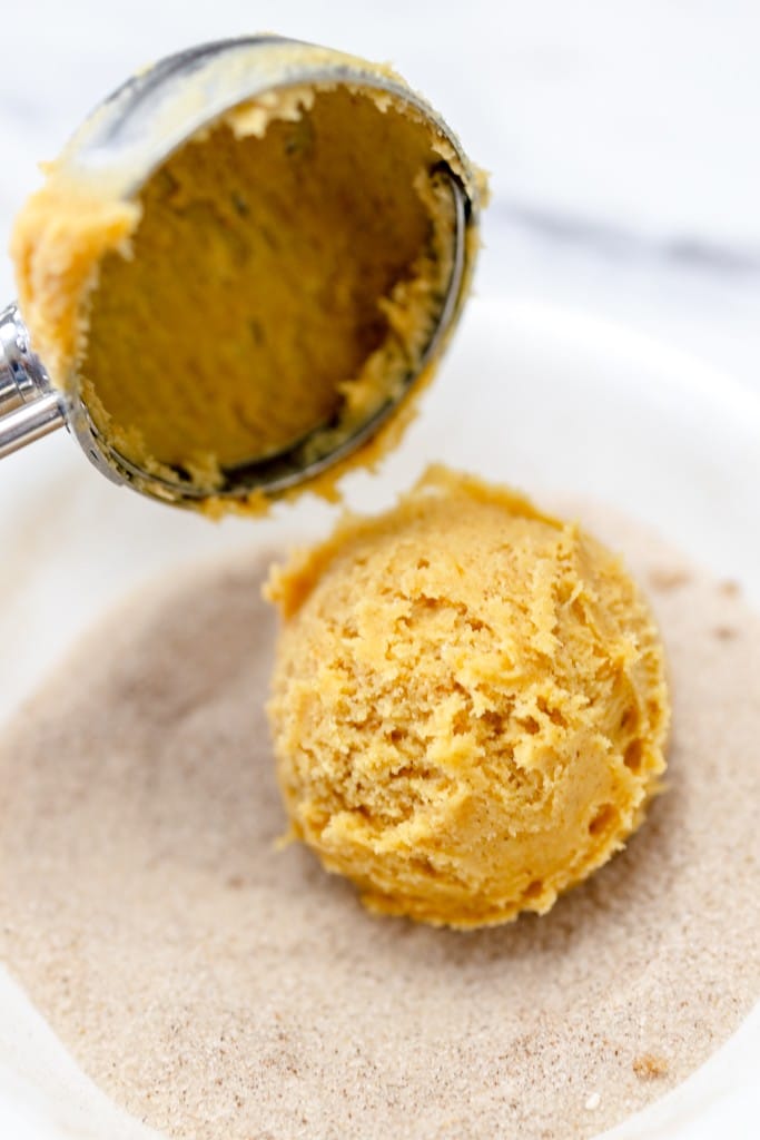 Close up of a pumpkin snickerdoodle cookie dough ball being put into the spiced sugar mixture.