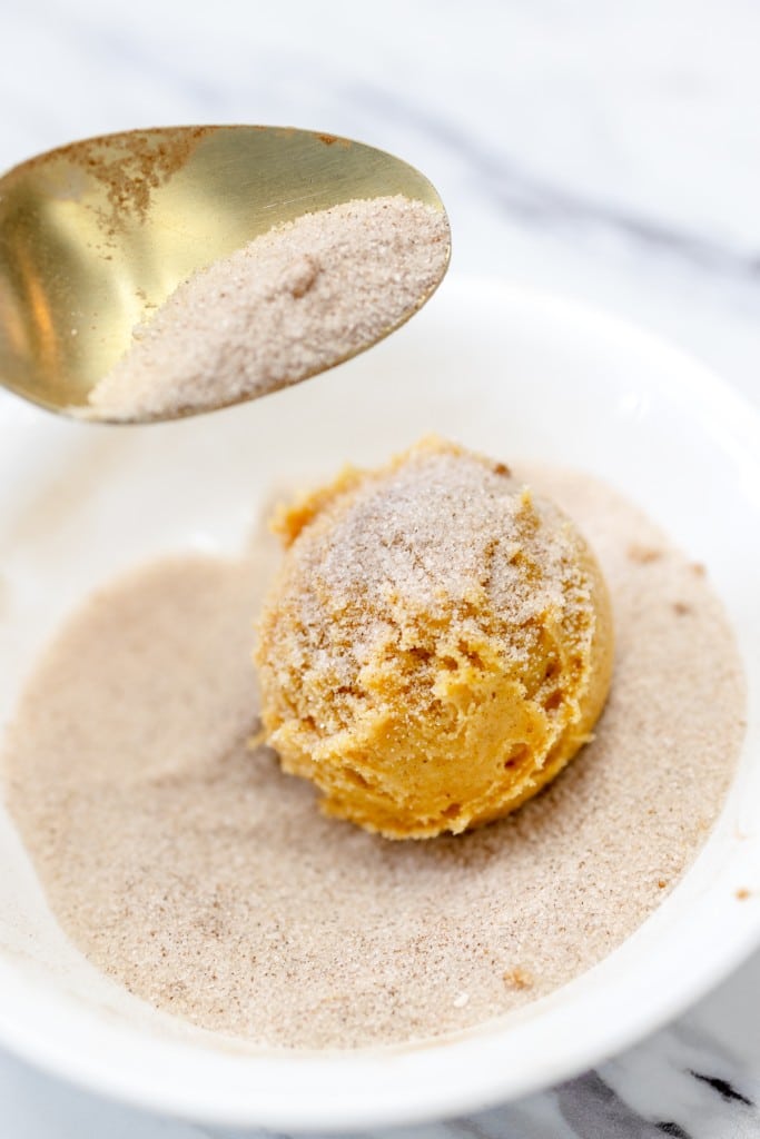 Close up of a pumpkin snickerdoodle cookie dough ball being coated with the spiced sugar mixture.