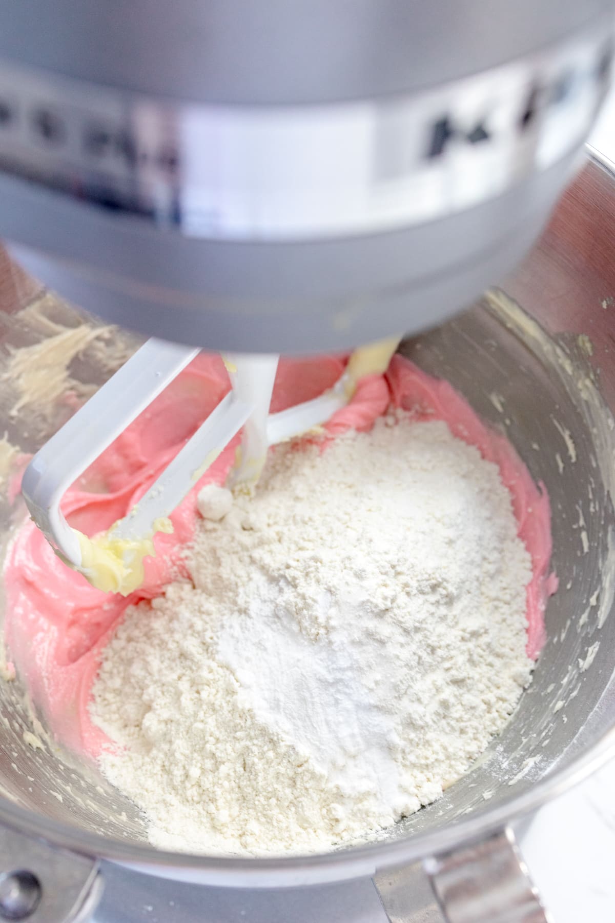 Close up of the bowl of a stand mixer with strawberry cookie dough in it with the flour added and ready to be mixed.