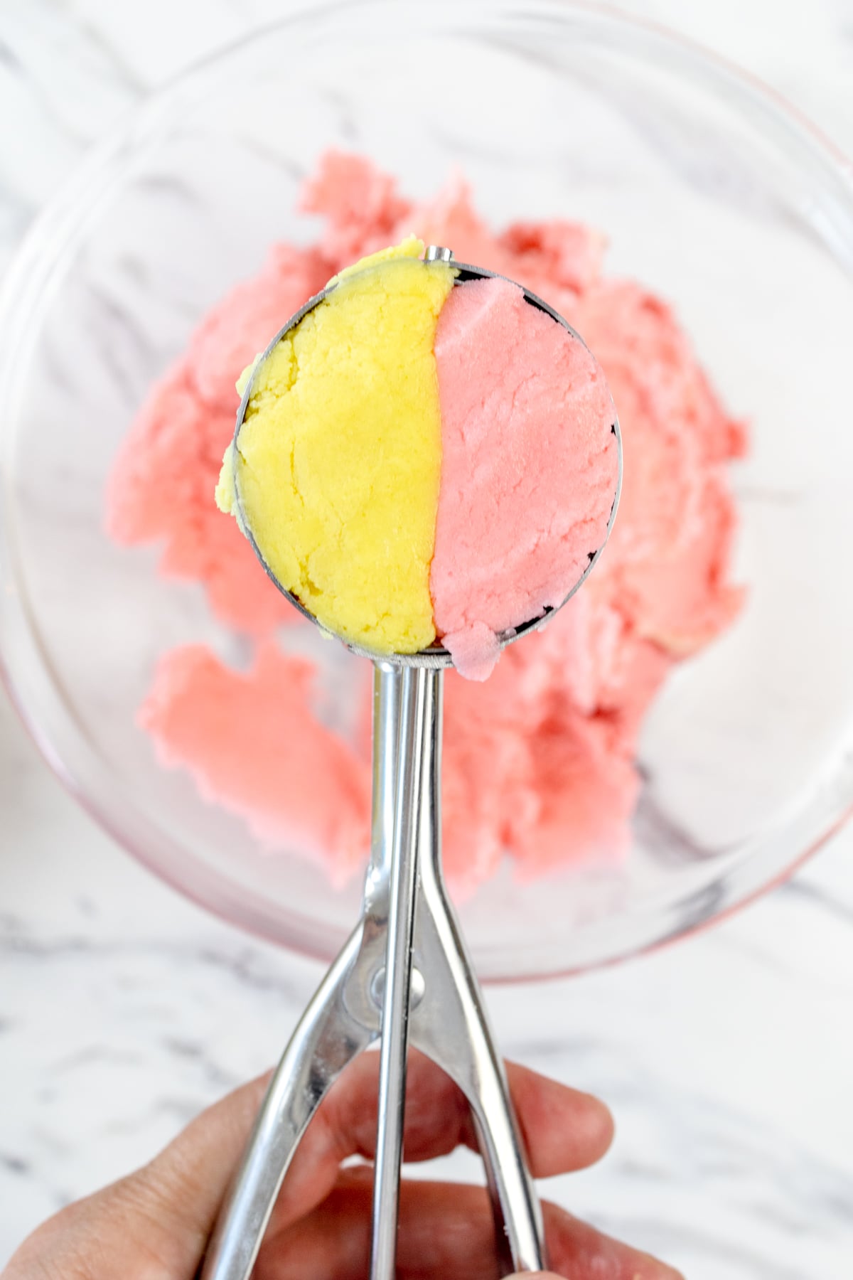 Close up of a cookies scoop which contains half lemon dough and half strawberry dough.