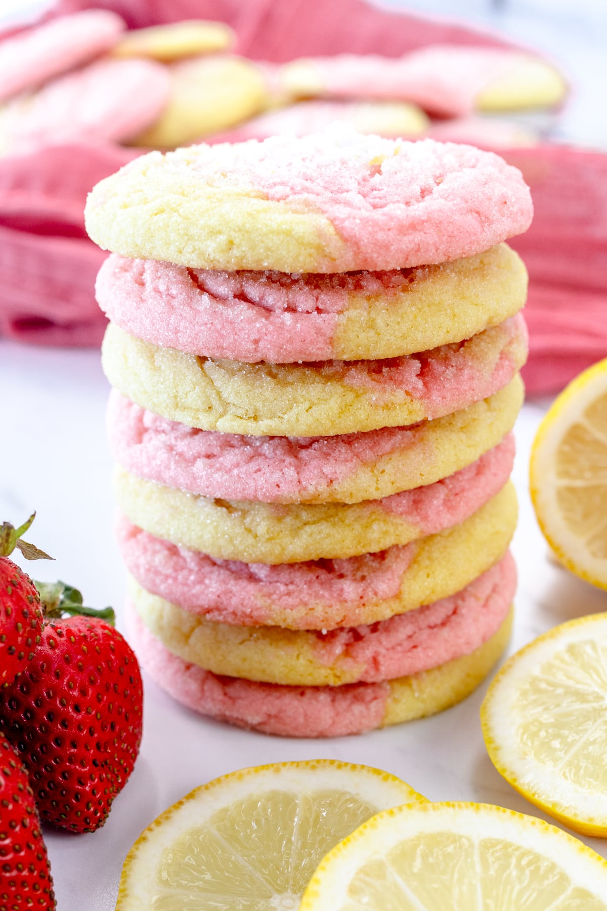 Close up view of Strawberry Lemonade Cookies on a grey surface, arranged in a stack, alongside strawberries and slices of lemon.