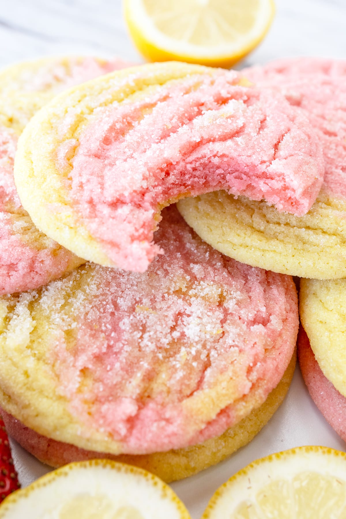 Close-up of Strawberry Lemonade Cookies on a grey surface, arranged in a pile alongside strawberries and slices of lemon.