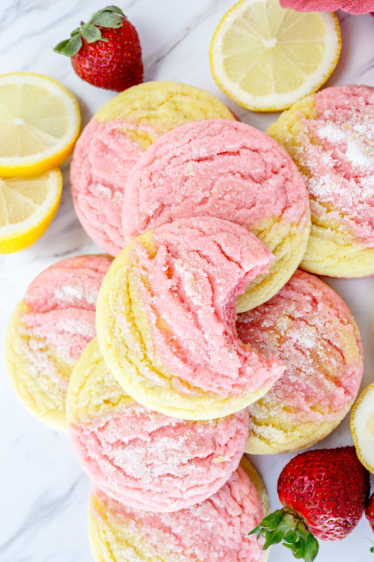 Top view of Strawberry Lemonade Cookies on a grey surface, arranged in a pile alongside strawberries and slices of lemon.