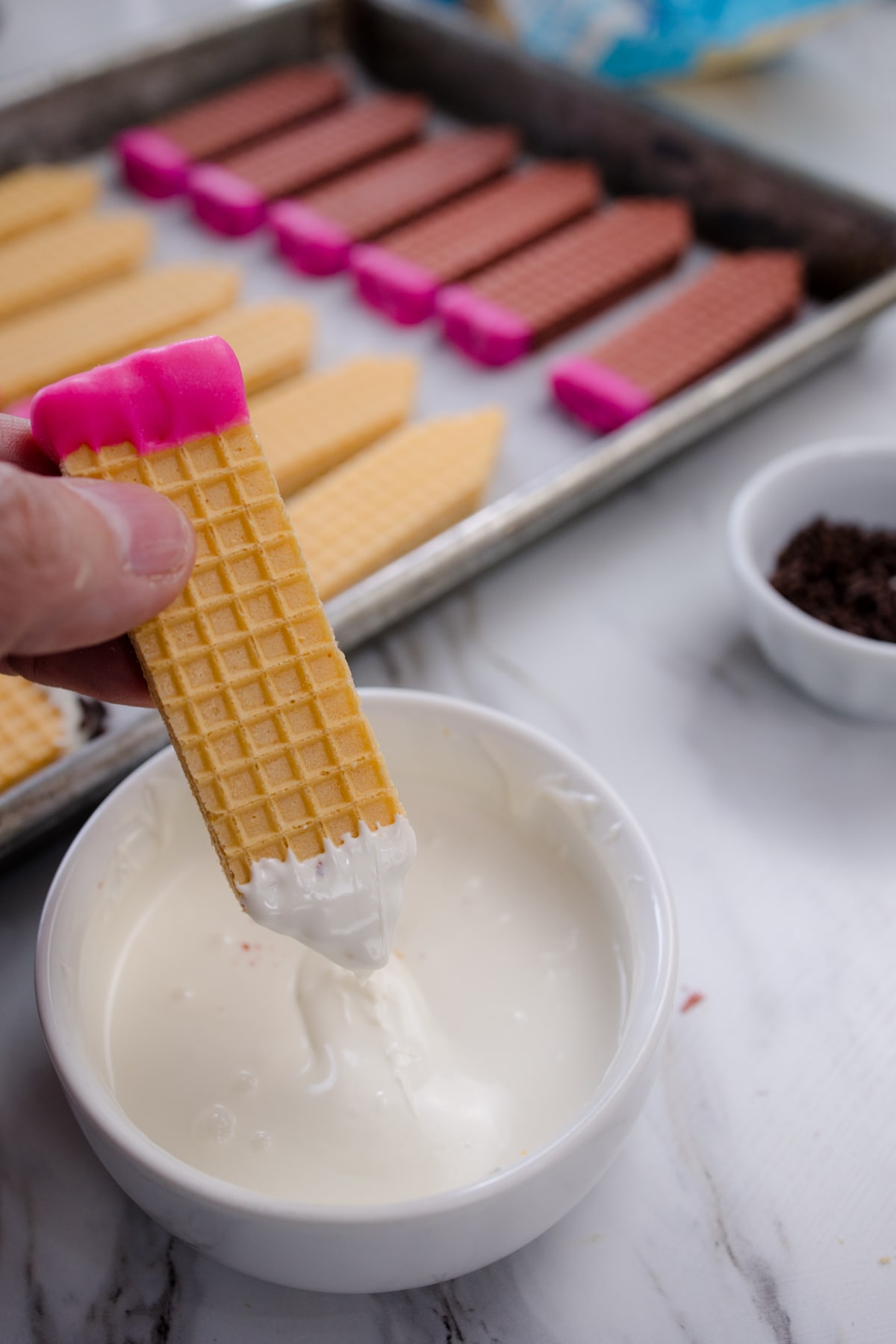 A hand dipping a wafer cookie into melted white chocolate.