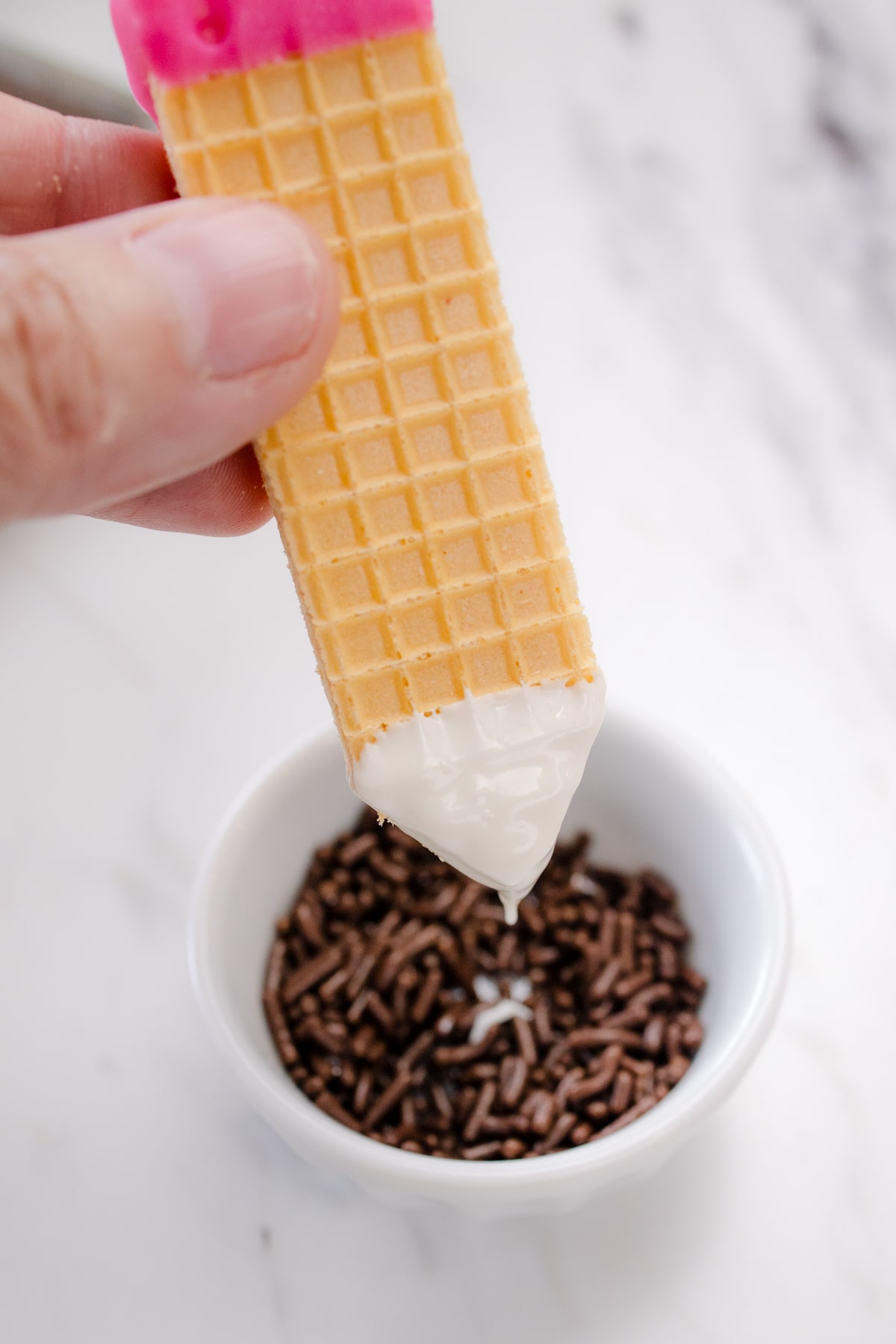 A hand dipping a wafer cookie into chocolate sprinkles.