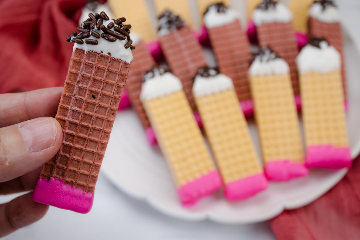 Pencil Wafer Cookies on a white plate, with a hand holding one of them.