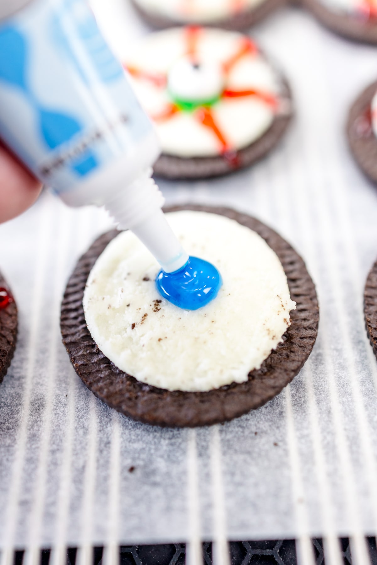Close up of blue icing being put in the center of half an oreo.