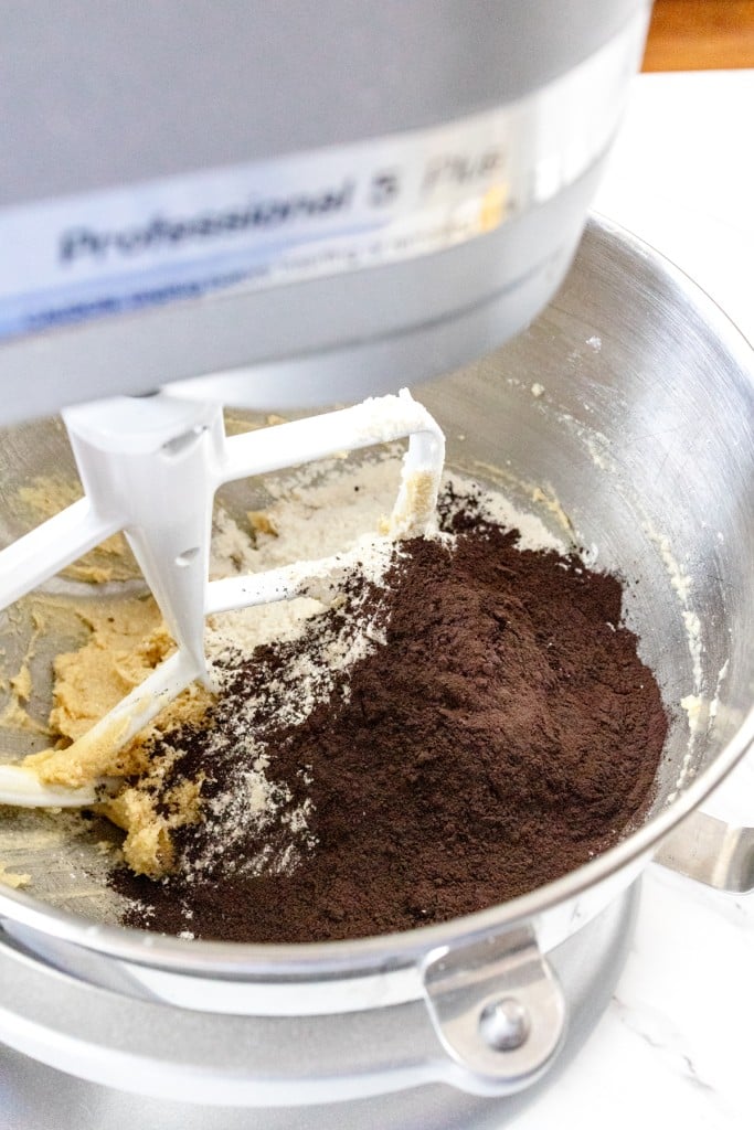 Close up of the bowl of a stand mixer with a paddle attachment mixing a creamed mixture with cocoa powder.