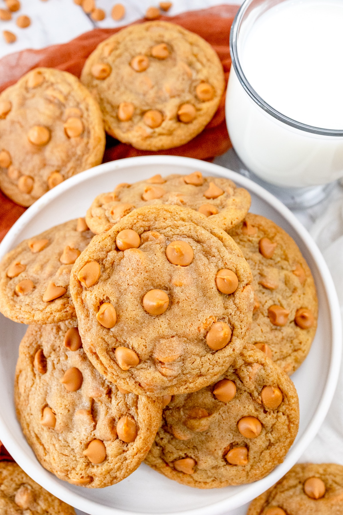 Top view of a plate of Butterscotch Chip Cookies, next to a glass of milk with other cookies around it.