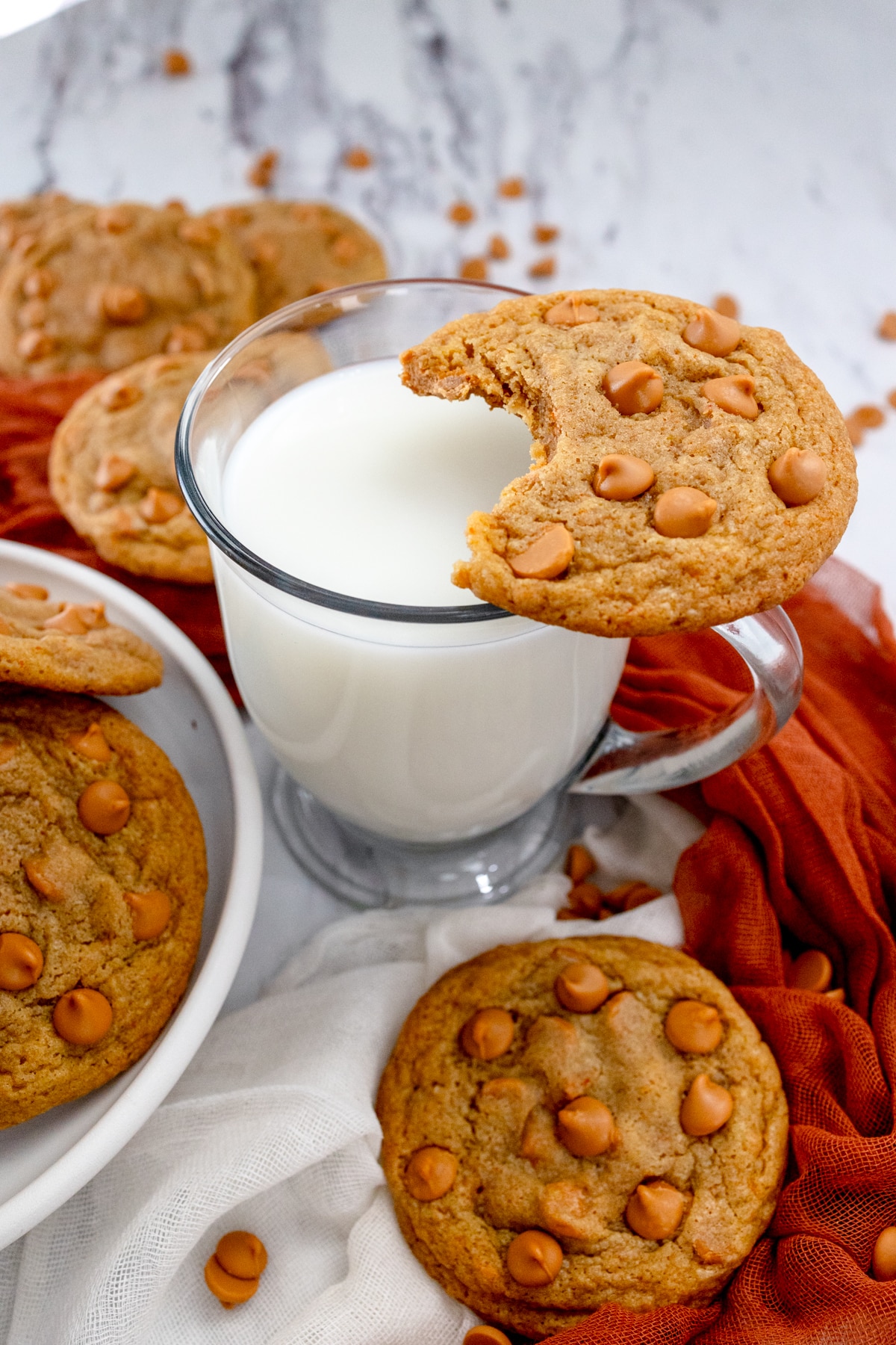Close up view of a butterscotch cookie resting on top of a glass of milk, with other cookies around the glass.