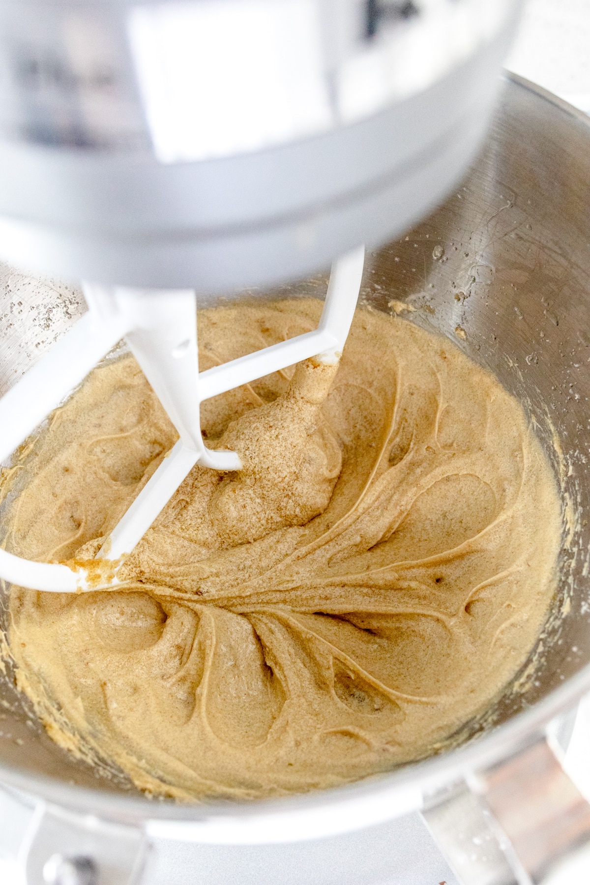 Close up of the bowl of a stand mixer with a paddle attachment mixing the cookie dough.