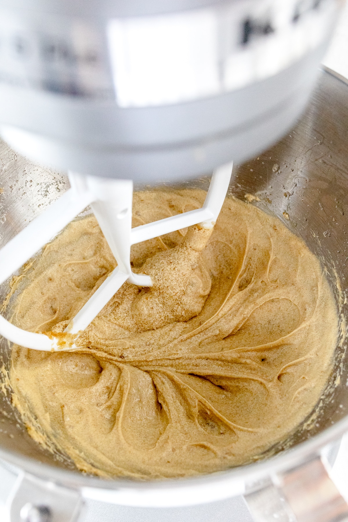 Close up of the bowl of a stand mixer with a paddle attachment mixing the cookie dough.