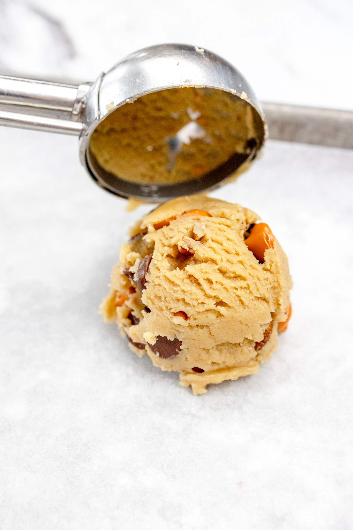 Close up of a cookie scoop placing a scoop of cookie dough onto a baking tray lined with parchment paper