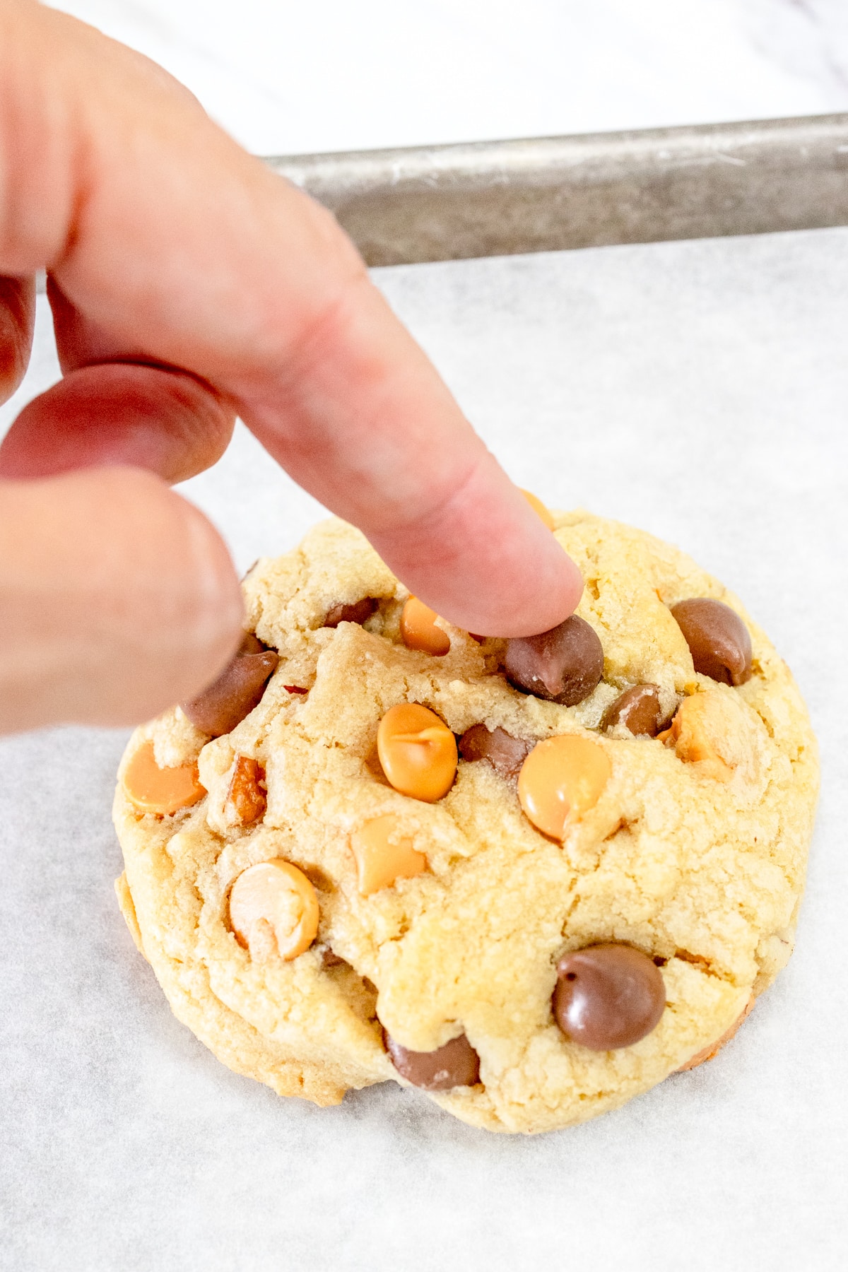 Close up of a hand gently pressing chocolate chips and butterscotch chips into a cookie before baking.