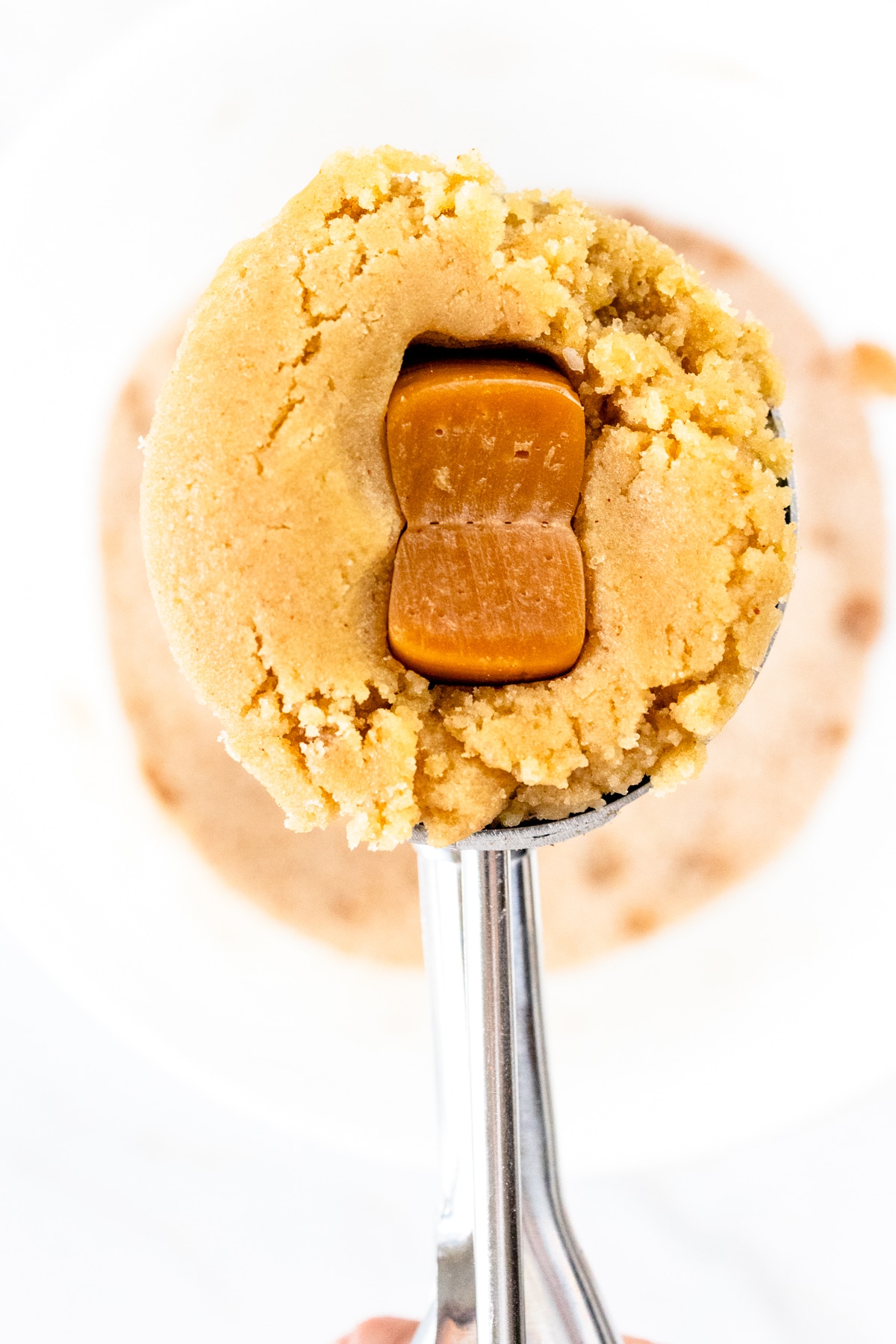 Close up of a cookie scoop filled with cookie dough that has a soft caramel pushed into the middle of it.
