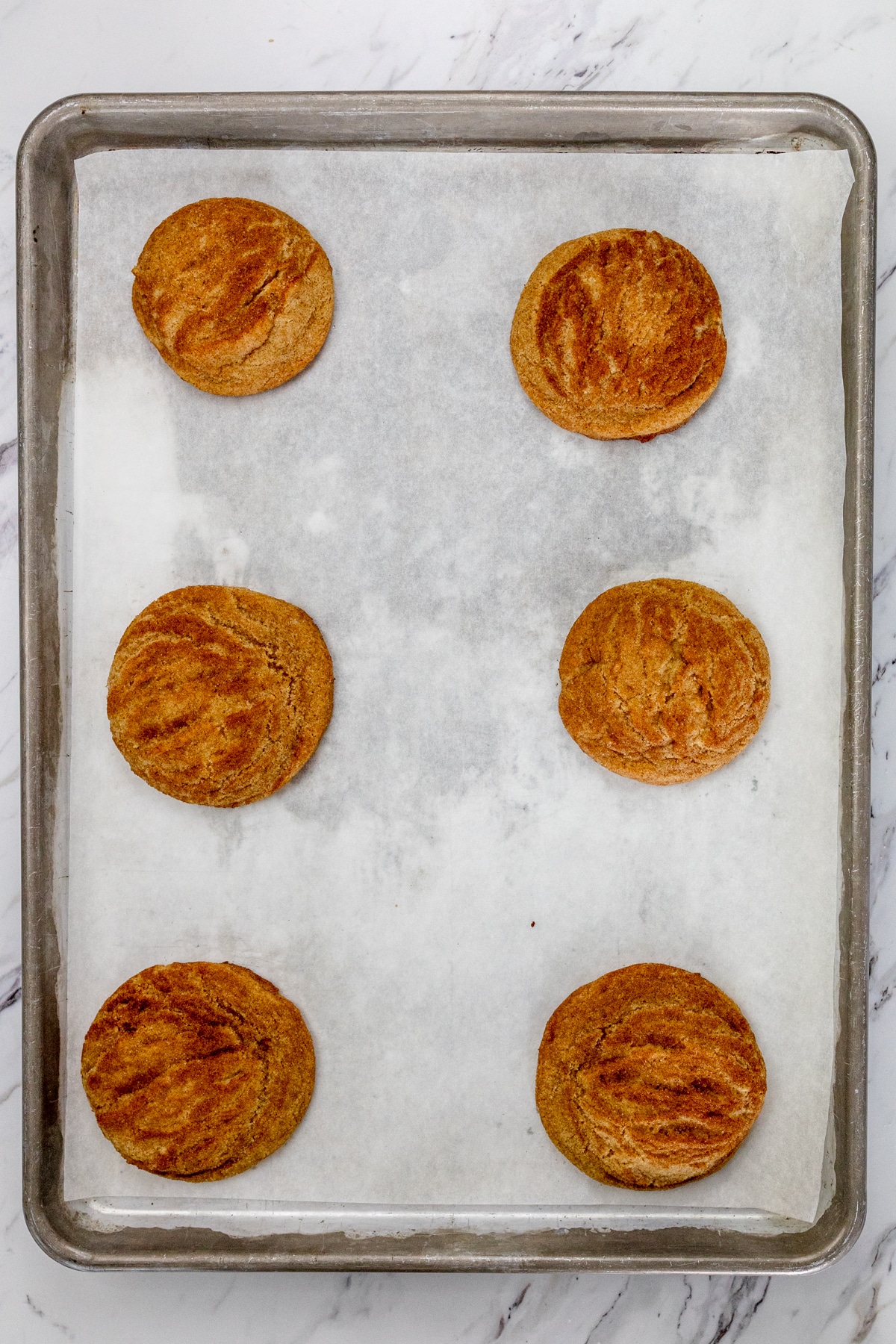 Top view of baking tray lined with parchment paper with baked Caramel Snickerdoodle Cookies on it.