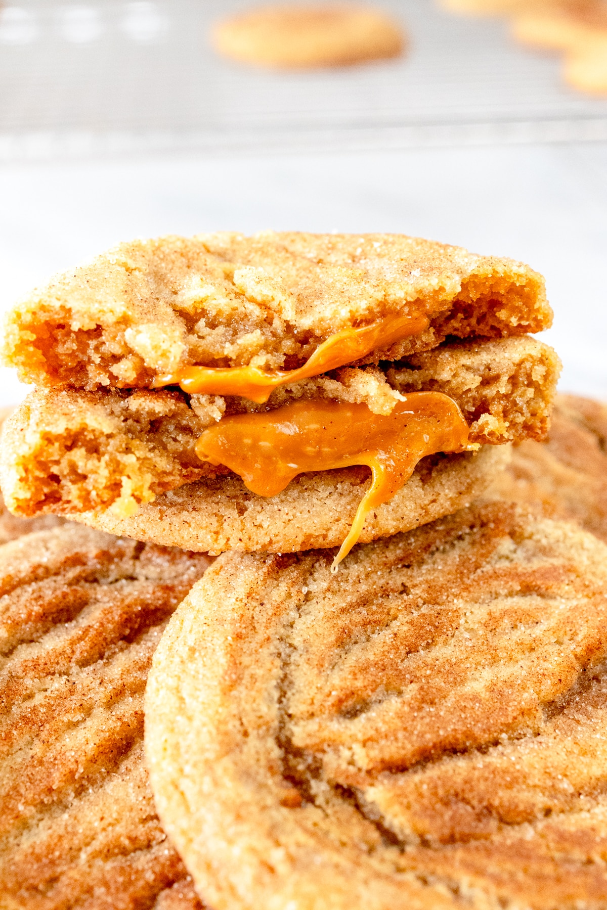 Close up of a Caramel Snickerdoodle Cookie broken in half on top of a pile of Caramel Snickerdoodle Cookies.