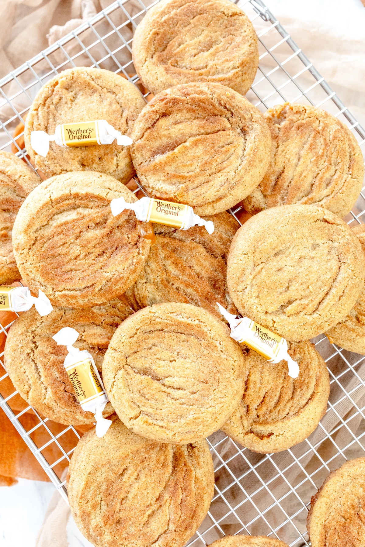 Top view of a pile of Caramel Snickerdoodle Cookies on a wire rack, with caramel candies interspersed throughout.