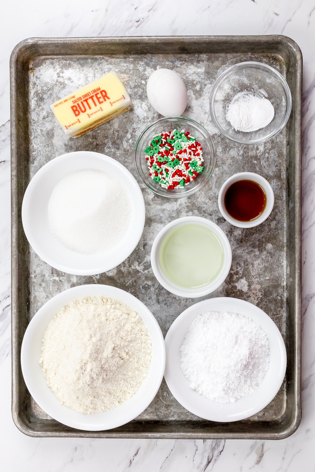 Top view of ingredients needed to make Christmas Sugar Cookies in small bowls on a baking tray.