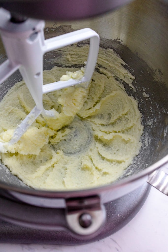 Close up of the bowl of a stand mixer with ingredients being mixed together with a paddle attachment.