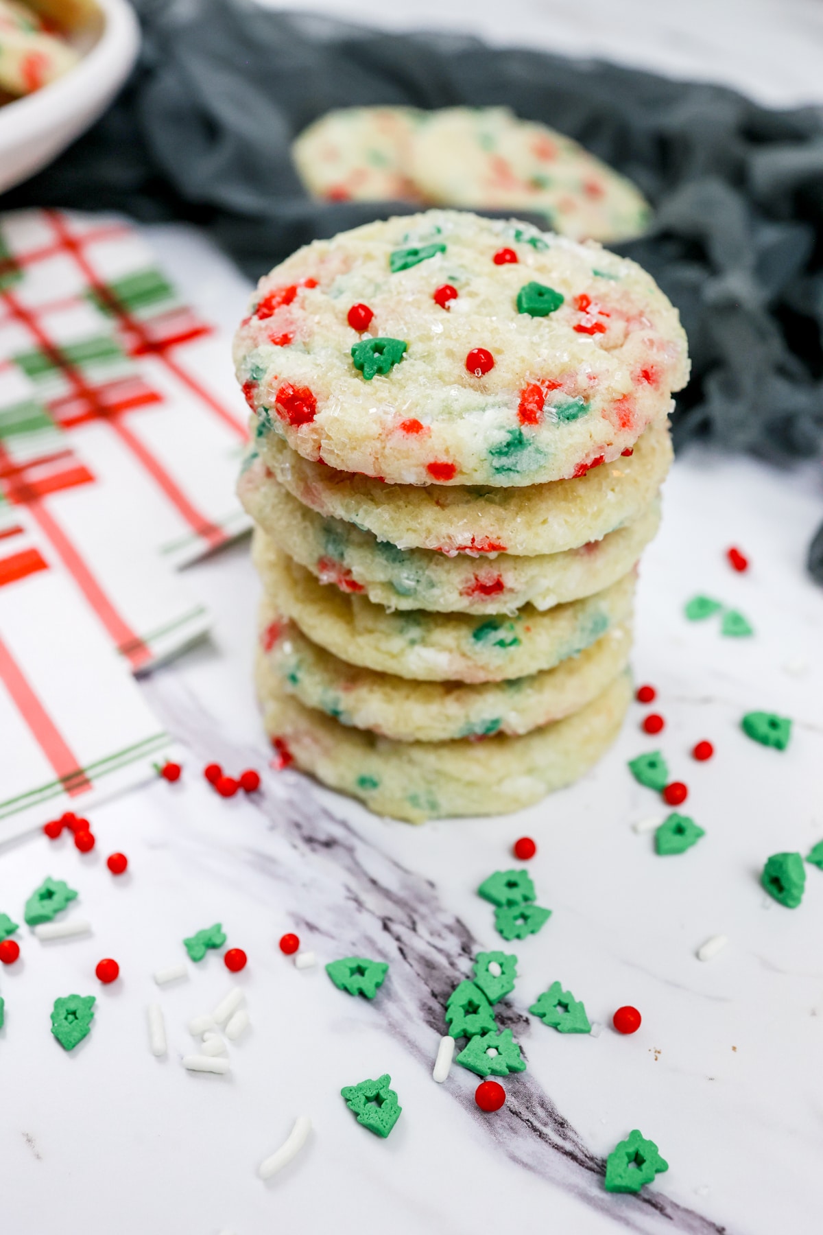 Close up of a stack of Christmas Sugar Cookies on a table with sprinkles around it.