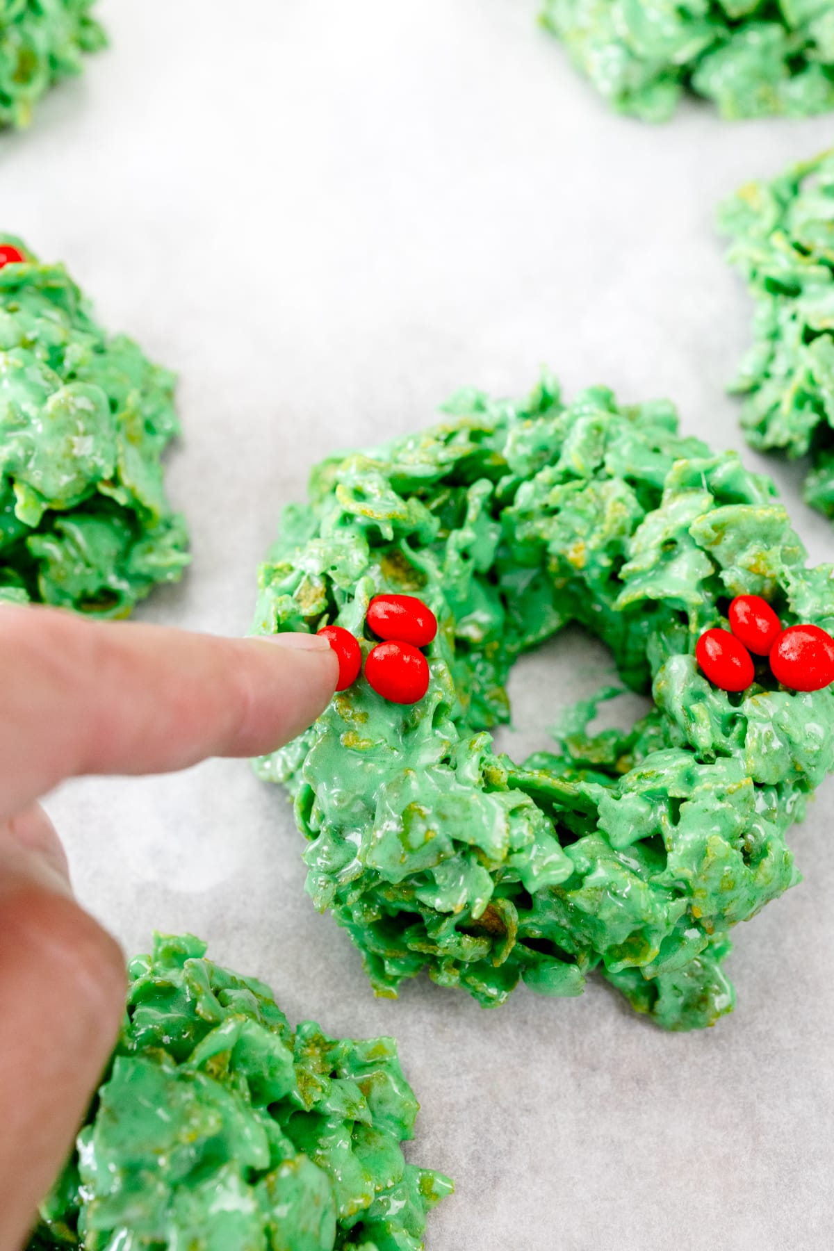 Close up of a finger pressing red candies into a Christmas Wreath Cookie.
