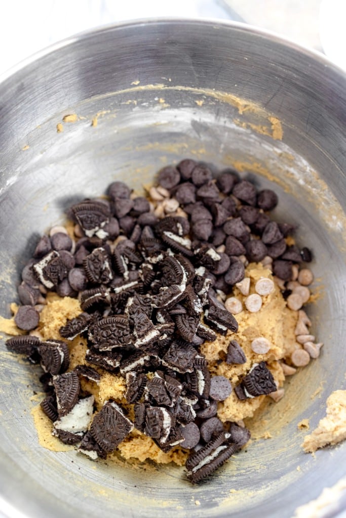 Close up of the bowl of a stand mixer with cookie dough in it with chopped oreos on top.