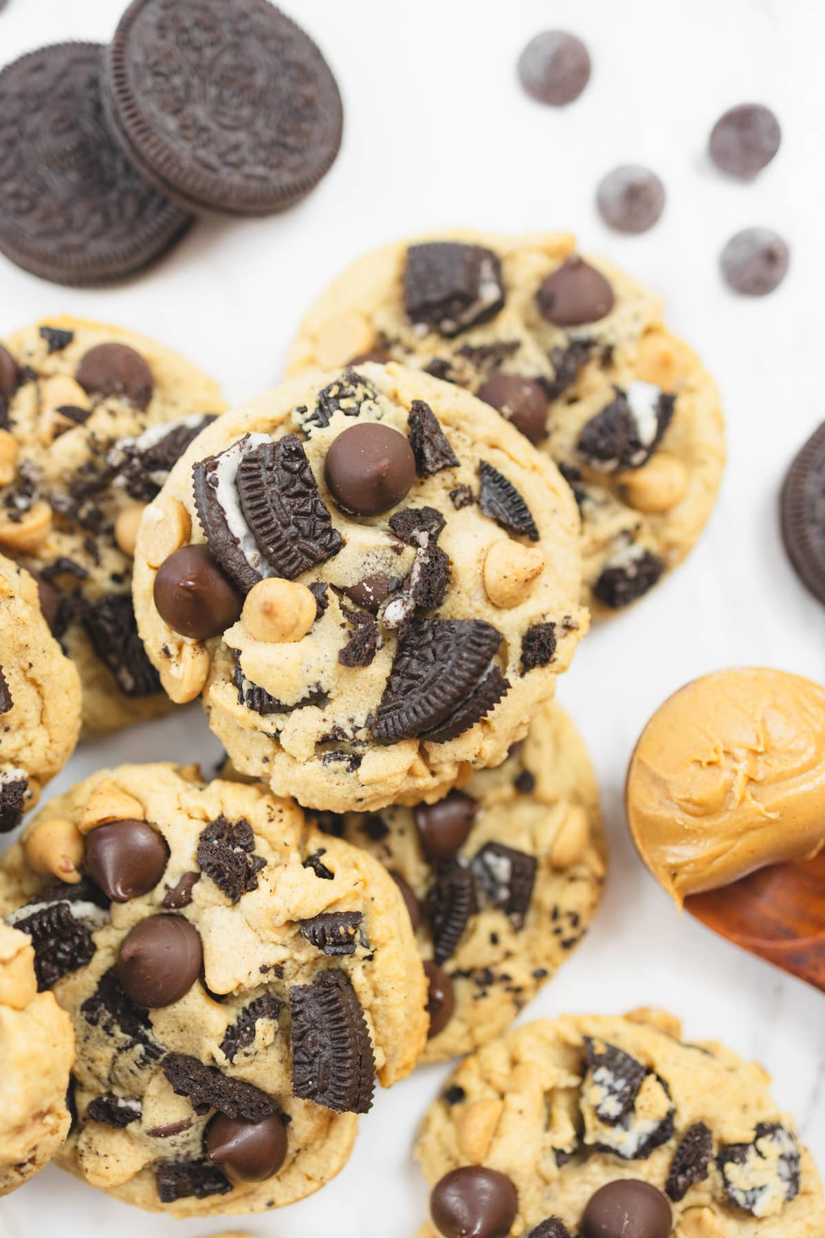 Top view of Peanut Butter Oreo Cookies on a white surface, surrounded by oreo cookies, chocolate chips, and a spoon with peanut butter in it.