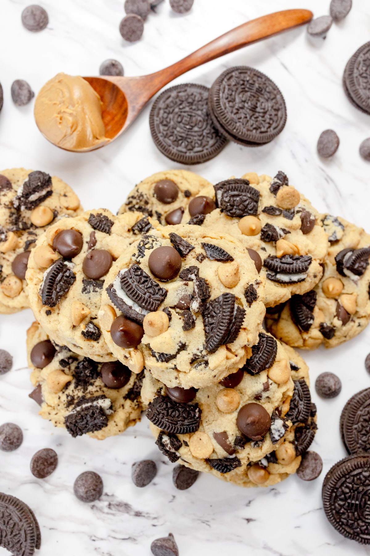Top view of Peanut Butter Oreo Cookies on a white surface, surrounded by oreo cookies, chocolate chips, and a spoon with peanut butter in it.