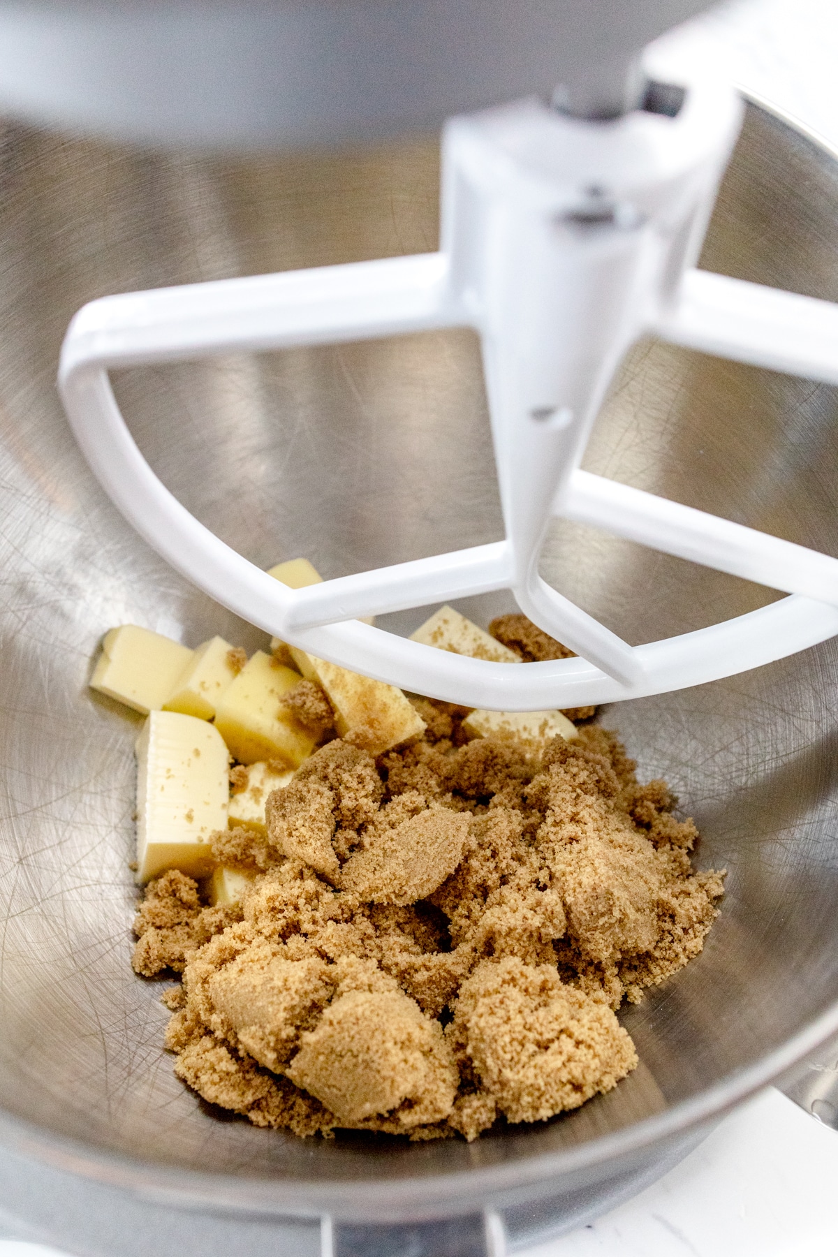 Close up of the bowl of a stand mixer with butter and brown sugar about to be creamed together with a paddle attachment.