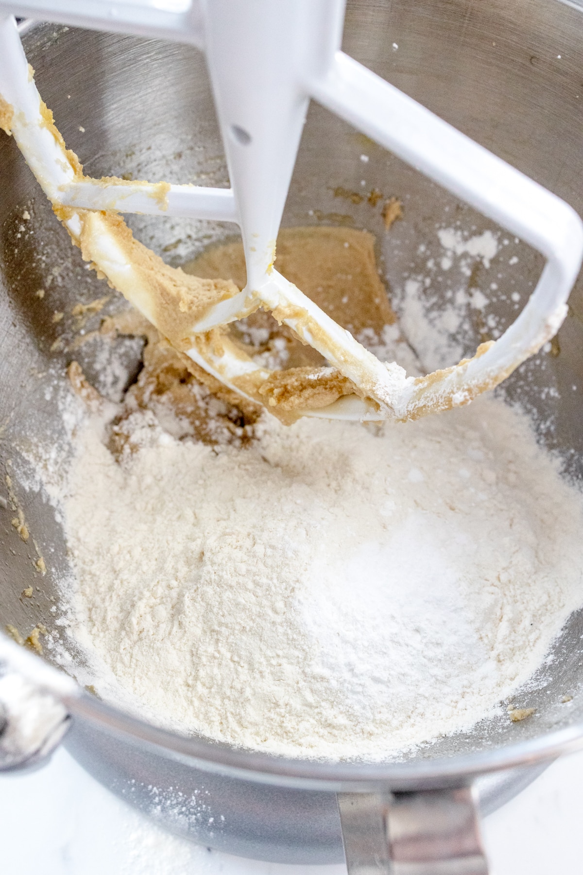 Close up of the bowl of a stand mixer with flour added to the butter and brown sugar mixture.