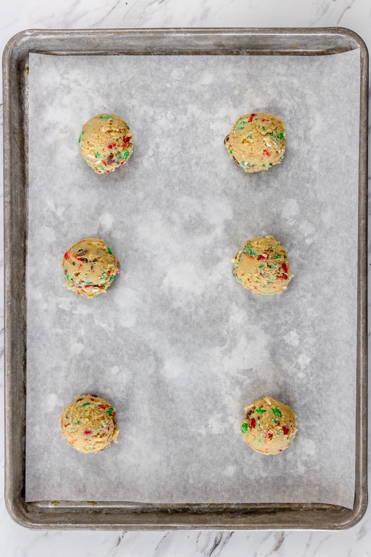 Top view of baking tray lined with parchment paper with cookie dough balls on it.