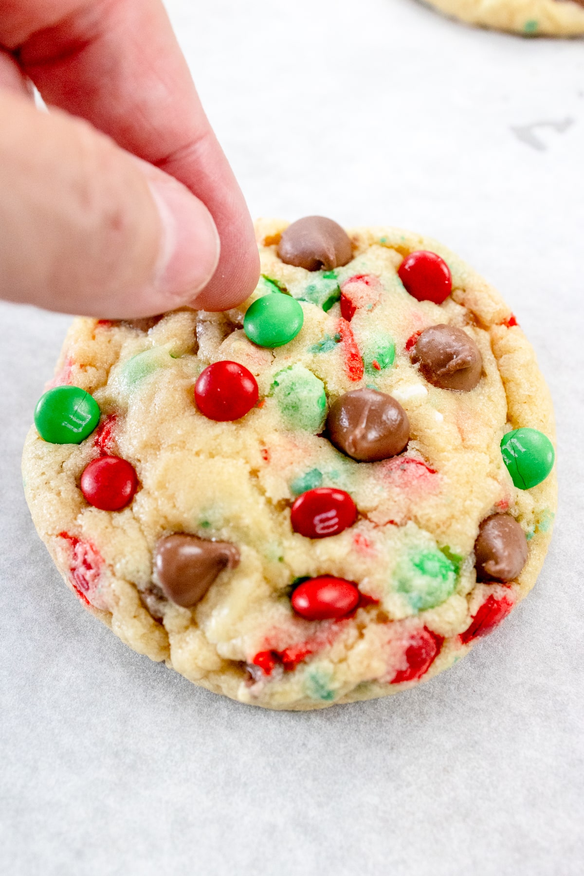 Close up of fingers pressing extra sprinkles into the top of a baked Santa Cookie.