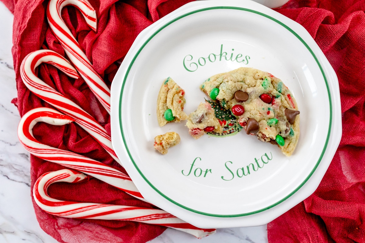 Top view of a Santa Cookie in broken pieces on a white plate, with candy canes around the plate.