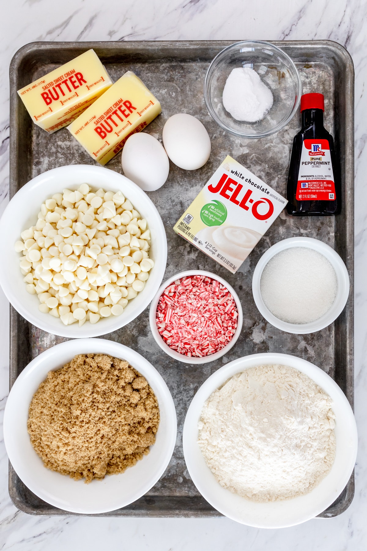 Top view of ingredients needed to make White Chocolate Peppermint Cookies in small bowls on a baking tray.